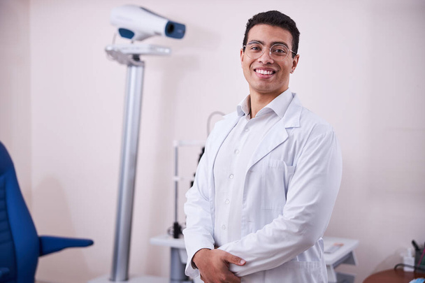 Cheerful bespectacled eye doctor standing in his office - Photo, Image