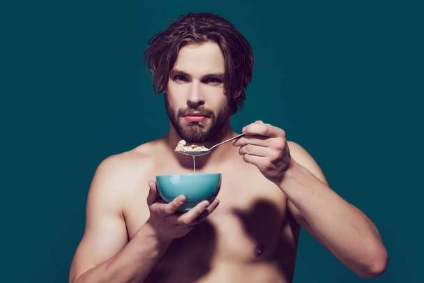 Morning healthy food and dieting, man with bare chest eating oatmeal. Breakfast cereal, healthy food for man or sport athlete. - Foto, immagini
