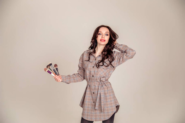 portrait of a beautiful young brunette with long hair. girl makeup artist holds makeup brushes in her hands. Beauty club concept. Copy space - Zdjęcie, obraz
