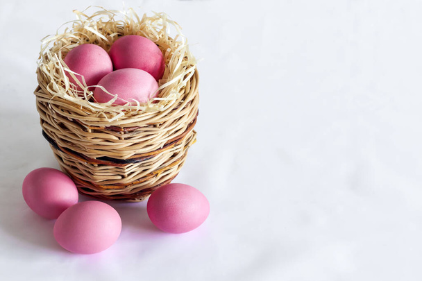 Minimalistic Easter composition with wicker basket and pink colored eggs on white background. Copy space - Фото, изображение