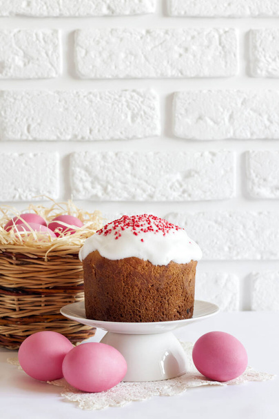 Minimalistic Easter composition with wicker basket with pink colored eggs and Easter cake on white background. Copy space - Fotografie, Obrázek