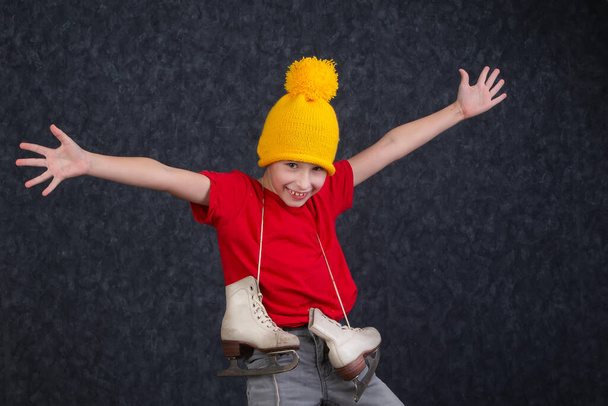 Handsome little boy in a knitted yellow hat with vintage skates on a gray background. - Photo, Image