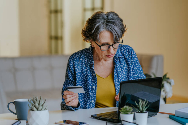 Portrait of senior stylish woman with grey hair making online shooping using laptop with credit card indoor. - Foto, Bild