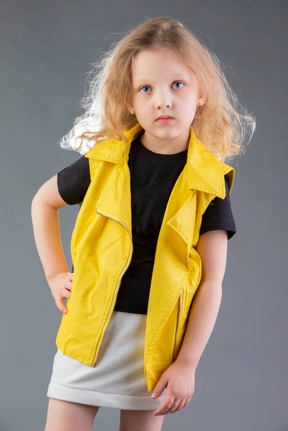 Gyönyörű szőke lány, sárga kabátban, szürke háttérrel. Öt éves kislány. Modellvizsgálatok gyermekek számára. - Fotó, kép