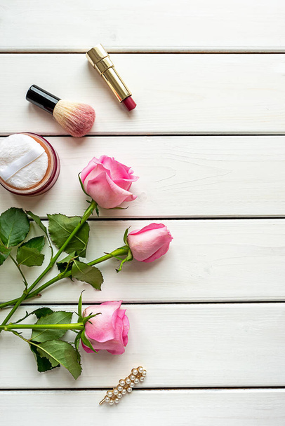 Bovenaanzicht met make-up, rozen, haarspeld en kopieerruimte op witte houten ondergrond - Foto, afbeelding