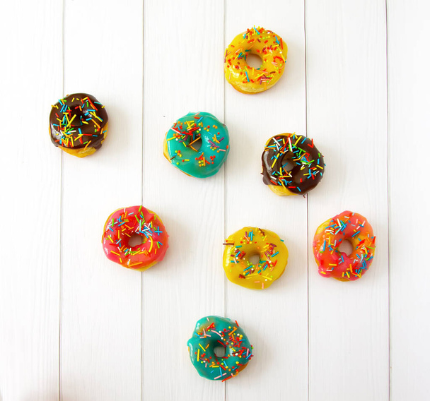 Homemade donuts with pink, blue, yellow and chocolate glaze with multicolored sugar sprinkles on a white wooden background. Bright background, selective focus - Photo, Image