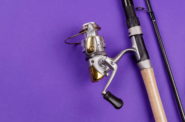 Fishing rod with attached fly fishing reel on blue background. Fishing, tackle, sport. Selective focus. - 写真・画像