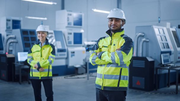 Portrait of Handsome Indian Engineer Wearing Safety Vest and Hardhat Crosses Arms and Smiles. Professional Woman Working in the Modern Manufacturing Factory. Facility with CNC Machinery and robot arm - Zdjęcie, obraz