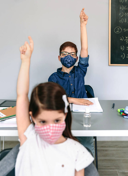 Students with masks raising hands at school - 写真・画像