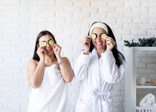 Spa- und Wellness-Konzept. Selbstversorgung. zwei schöne Frauen bei Wellness-Behandlungen, die Augen mit Gurken bedecken - Foto, Bild