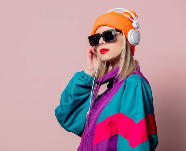 スタイルの女の子で80年代のスポーツスーツとサングラスでヘッドフォンでピンクの背景 - 写真・画像