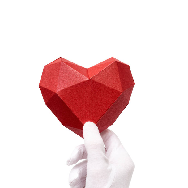 Red polygonal paper heart in hand with white fabric glove isolatwd on white background. Healthcare and medical concept. - 写真・画像