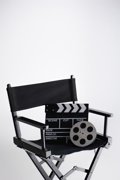 clapperboard και ταινία κύλινδρο σε καρέκλα σκηνοθέτη σε λευκό με χώρο αντιγραφής, κινηματογραφική έννοια - Φωτογραφία, εικόνα