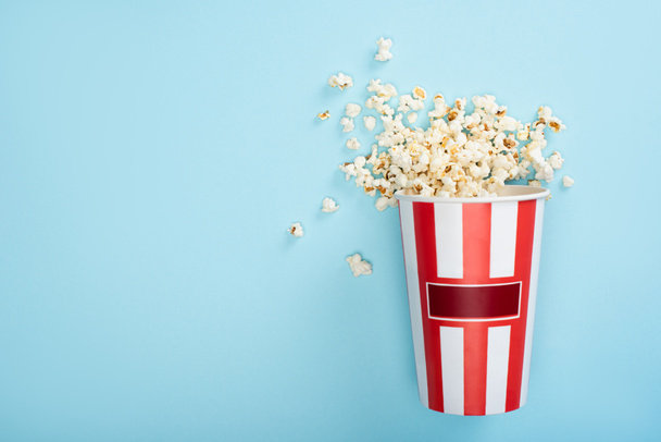 pohled shora na proužkovaný kartónový kbelík s popcornem na modré, koncepce kina - Fotografie, Obrázek