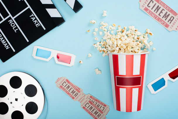 shora pohled na clapperboard, 3D brýle, vstupenky do kina, film naviják a kbelík popcornu na modré - Fotografie, Obrázek