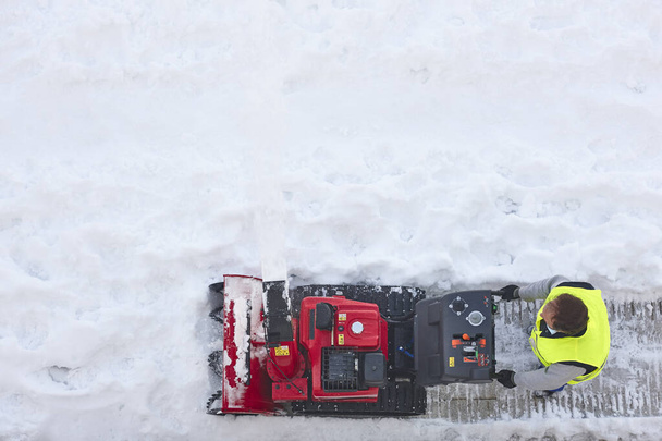 Εργάτης καθαρίζει χιόνι στο πεζοδρόμιο με ένα φυσητήρα χιονιού. Συντήρηση - Φωτογραφία, εικόνα