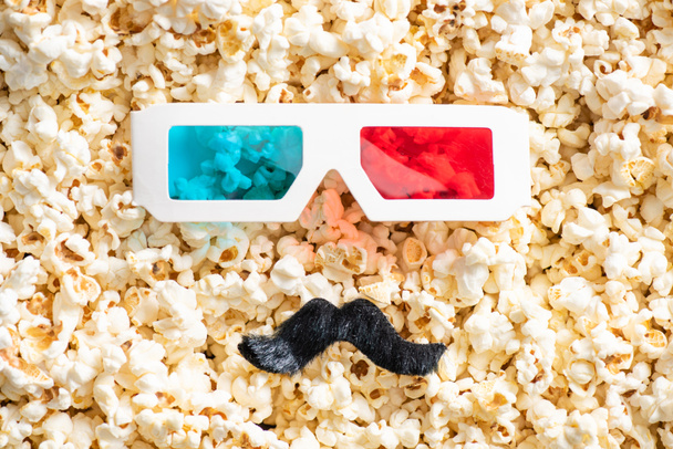 top view of 3d glasses and artificial mustache on scattered popcorn, cinema concept - Photo, Image