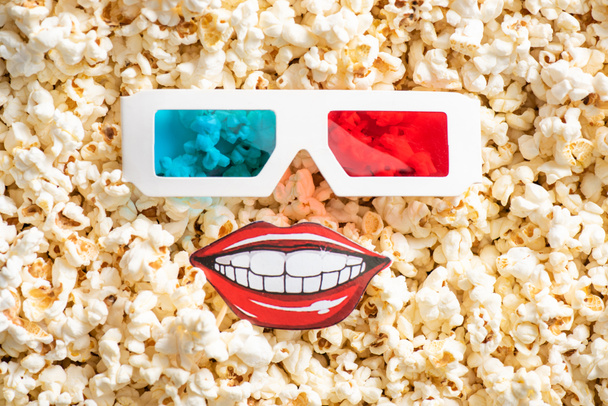vue du dessus des verres 3D et de la bouche souriante de papier coupé sur le pop-corn croustillant, concept de cinéma - Photo, image