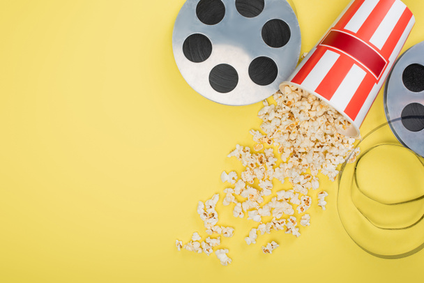 top view of film reels near bucket with scattered popcorn on yellow, cinema concept - Photo, Image