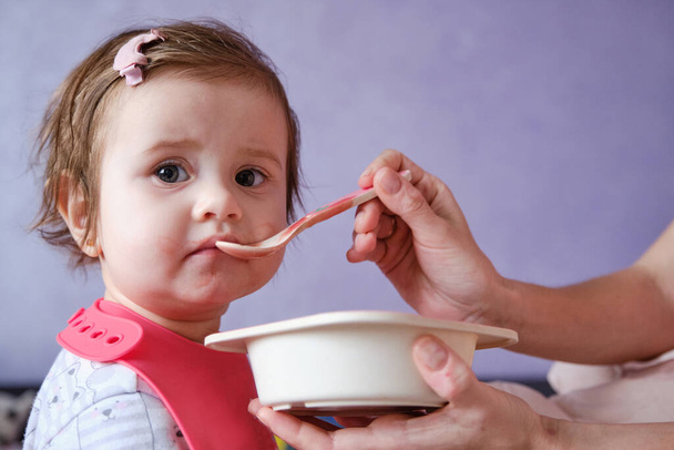 Een meisje van een jaar dat soep eet. Moeder geeft babyvoeding van een lepel. Close-up portret - Foto, afbeelding