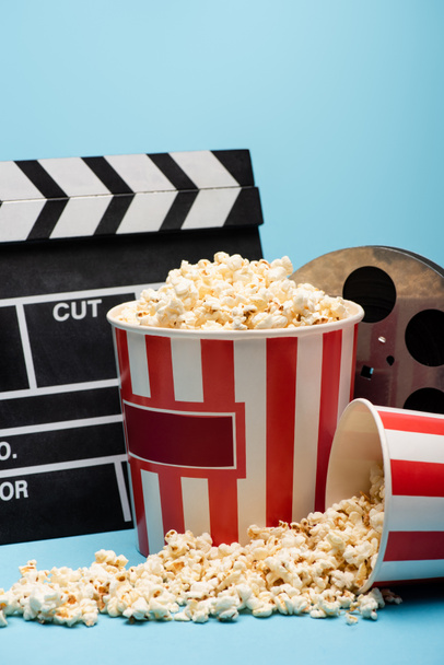kbelíky popcornu, clapperboardu a filmové cívky na modré, koncepce kina - Fotografie, Obrázek