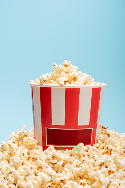 secchio a strisce e mucchio di gustosi popcorn isolati su blu, concetto di cinema - Foto, immagini