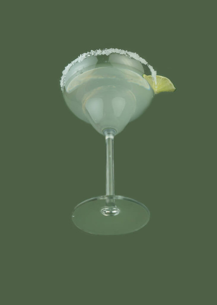 Glass of cocktail margarita with salt and a slice of lime on a green background. National margarita day concept. - Photo, Image