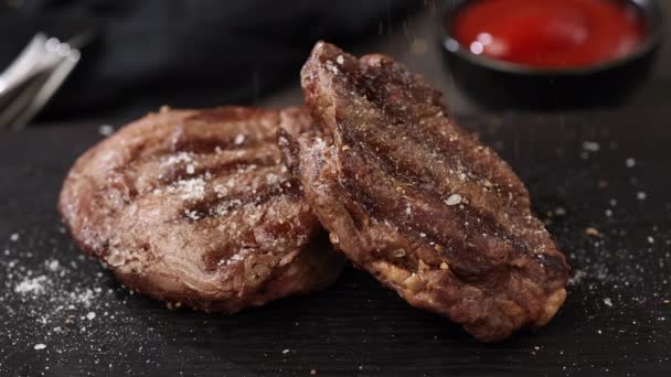 pepř padající na čerstvě grilované hovězí řízek steak maso na černém kameni restaurace talíř. přidat tymián zpomalit - Záběry, video