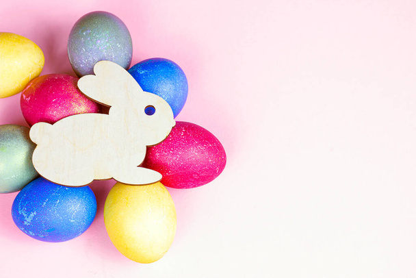 Top view flat lay funny wooden Easter Bunny with colorful eggs as symbols of a holiday with copy space on light pink background. - Photo, Image