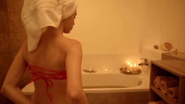 vrouw met handdoek op hoofd invoeren badkamer met bad  - Video