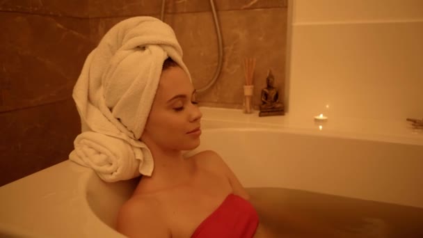 довольная женщина с полотенцем на голове расслабляющий и улыбаясь в ванной  - Кадры, видео