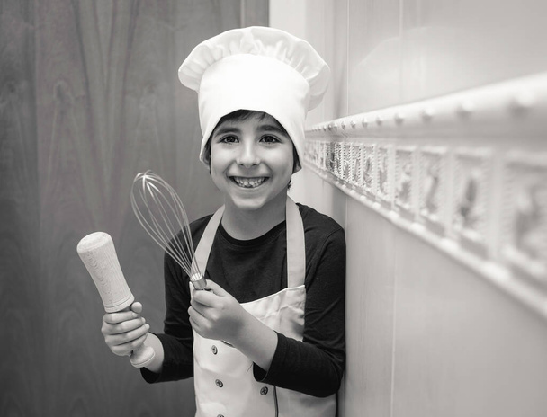 笑顔の少年はシェフの制服で彼の家の台所でポーズライフスタイル、家庭生活、閉じ込めと新しい通常の概念 - 写真・画像
