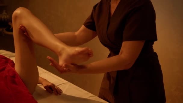 μασέρ ανύψωση πόδι της νεαρής γυναίκας, ενώ κάνει μασάζ  - Πλάνα, βίντεο