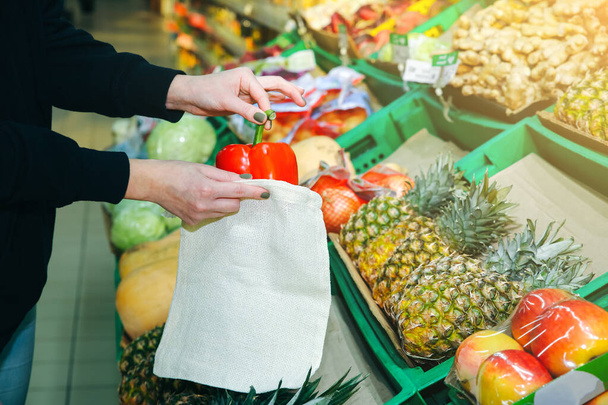 Woman is putting vegetables in reusable shopping bag. Ecologically and environmentally friendly packets. Canvas and linen fabrics. Save nature concept. No plastic single use in supermarkets. - Foto, Imagen