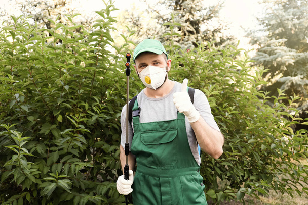 Worker with insecticide sprayer near green bush outdoors. Pest control - Fotó, kép