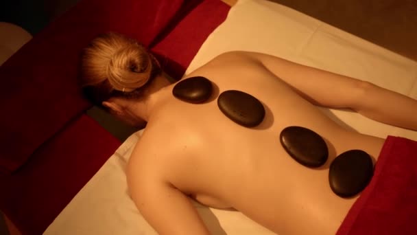 πίσω όψη της γυναίκας που λαμβάνει ζεστό μασάζ πέτρα στο σαλόνι σπα - Πλάνα, βίντεο