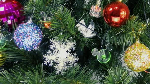 Auf einem hellen Hintergrund blinkende Glühbirnen und bunte Dekorationen auf einem grünen Weihnachtsbaum - Filmmaterial, Video