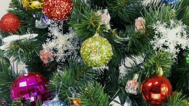Bombillas intermitentes y juguetes coloridos en un árbol de Navidad verde sobre un fondo claro - Metraje, vídeo