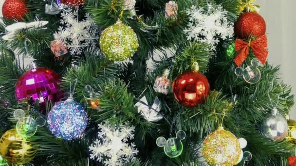 Bombillas intermitentes y decoraciones coloridas en un árbol de Navidad sobre un fondo claro - Metraje, vídeo
