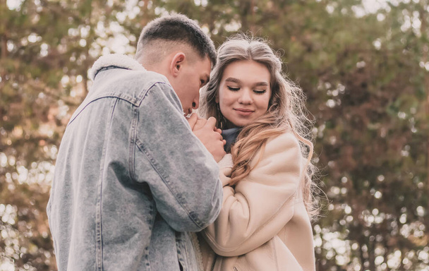 хлопець тримає дівчину за руки і цілує їх, а дівчина посміхається, перебуваючи в сосновому лісі взимку
 - Фото, зображення
