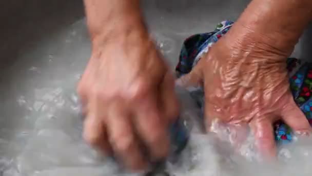 Les mains ridées âgées de femme métissée froisser robe textile colorée tandis que lavage à la main blanchisserie - Séquence, vidéo