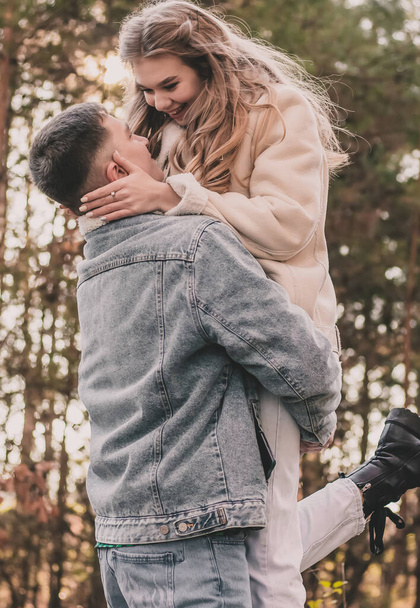Het meisje sprong in de armen van de man, houdt zijn gezicht vast met haar handen en glimlacht in het dennenbos - Foto, afbeelding