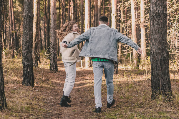a girl and a guy are holding hands walking and having fun in a pine forest - Photo, Image