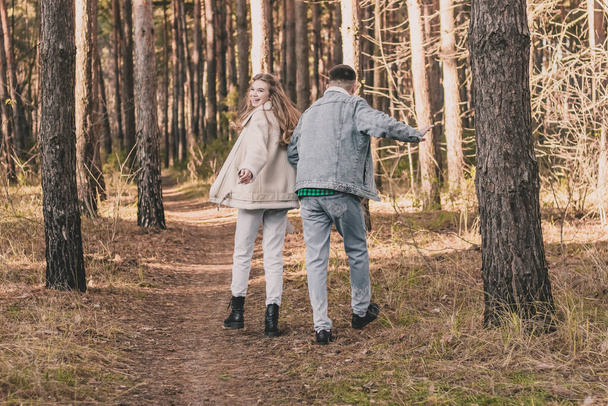 una chica y un chico están tomados de la mano caminando y divirtiéndose en un bosque de pinos - Foto, Imagen