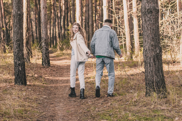 a girl and a guy are holding hands walking and having fun in a pine forest - Foto, Bild