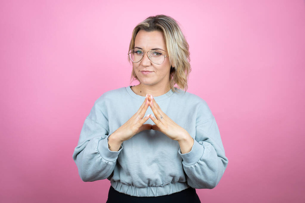Young caucasian woman wearing sweatshirt over pink background with Hands together and fingers crossed smiling relaxed and cheerful. Success and optimistic - Photo, Image