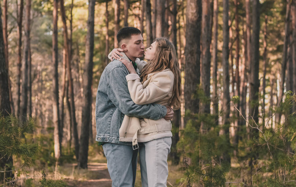 el chico abraza a la chica firmemente y la besa mientras está en el bosque de pinos - Foto, imagen