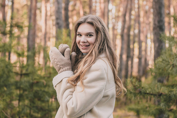 nuori tyttö mallin ulkonäkö mäntymetsässä on pukeutunut turkistakkiin ja lämmin villapaita näyttää kädet lapasissa ja hymyissä - Valokuva, kuva