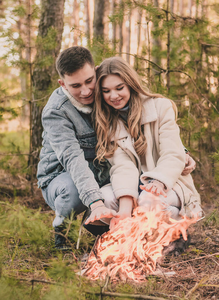pareja calienta sus manos cerca de un fuego en un bosque de pinos en invierno - Foto, imagen