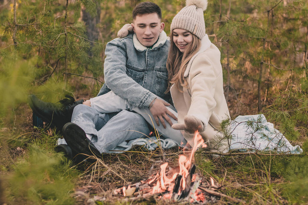 koppel op een picknick in een dennenbos koesteren in de buurt van het vuur - Foto, afbeelding